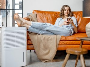 A woman relaxing on an orange couch next to a portable air purifier