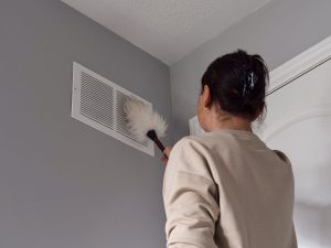 A woman is dusting off her air ducts for cleaning maintenance