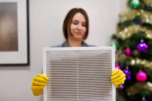 An image of a woman holding a dirty air filter with a Christmas tree in the background